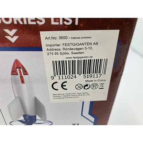 Rachetă de jucărie din spumă albă, cu o înălțime de aproximativ 30 cm, prevăzută cu o bază de elice din plastic roșu, alimentată cu un cablu USB, inclusiv o telecomandă și o rampă de lansare albastră.