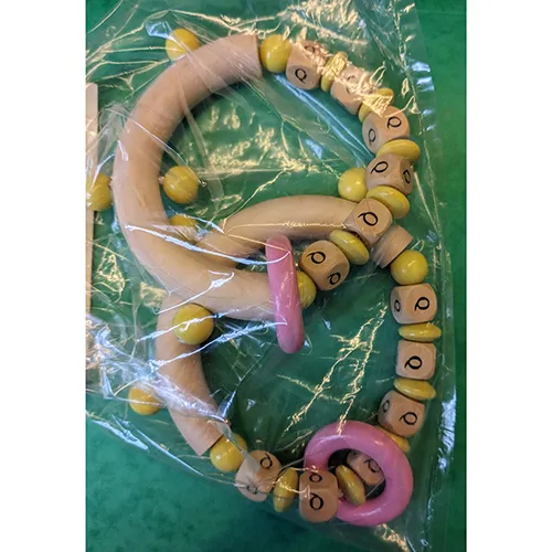 Jucărie din lemn cu margele galbene, un inel roz și literele numelui marcate pe cuburi.