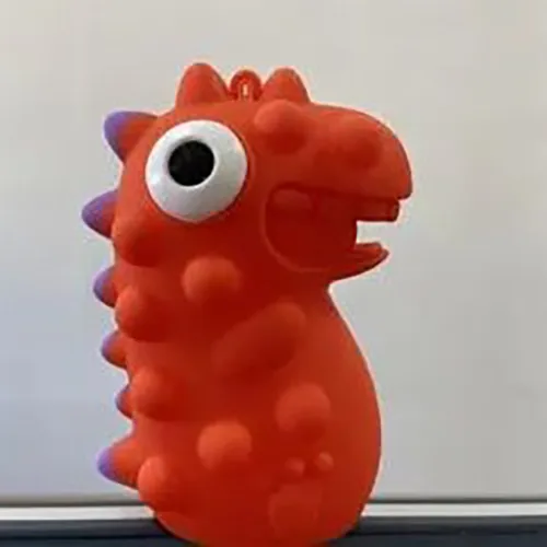 Jucărie din plastic de culoare roșie moale, care conține un LED, cu o creastă purpurie și ochi alb-negru care ies din cap atunci când jucăria este stoarsă.