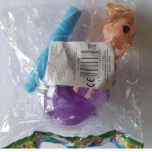 Păpușă de plastic într-o rochie textilă purpurie. Picioarele păpușii sunt plasate într-o minge de plastic transparentă cu pene. Un controler, inclusiv o baterie, este atașat la capul păpușii.