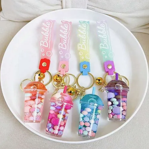 Trei brelocuri cu o figură de ceașcă de ceai cu bule. Figura din plastic conține două lichide neamestecabile (roz și limpede) în recipiente sigilate cu un dop din plastic de cauciuc. Produs vândut online, în special prin intermediul Shein (identificator de produs, SKU: sc2407277808880181).