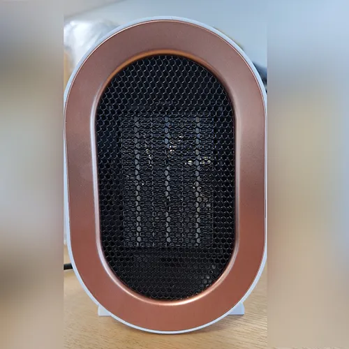 Încălzitor cu ventilator de culoare albă, de formă ovală, prevăzut cu o grilă neagră și un cablu de alimentare de culoare neagră. Produs vândut online, în special prin intermediul Amazon (ASIN: B0CMCZT6QR).