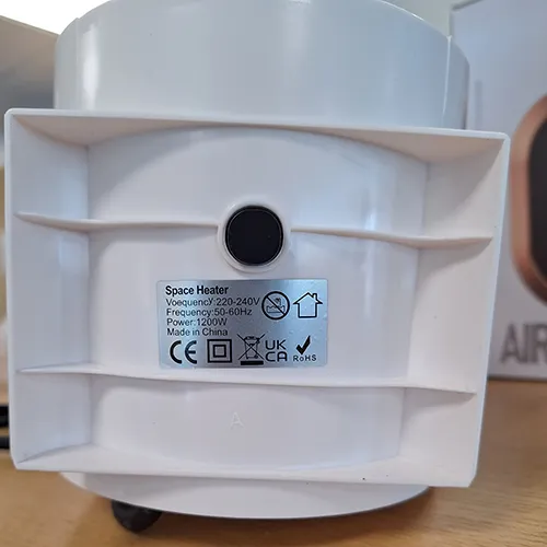 Încălzitor cu ventilator de culoare albă, de formă ovală, prevăzut cu o grilă neagră și un cablu de alimentare de culoare neagră. Produs vândut online, în special prin intermediul Amazon (ASIN: B0CMCZT6QR).