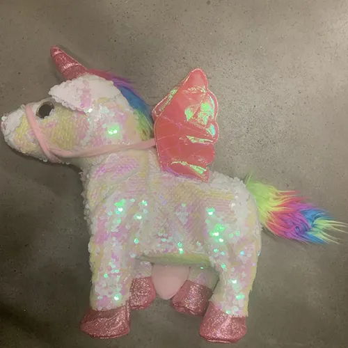 Unicorn de jucărie alimentat cu baterii, cu o suprafață textilă cu cântare reversibile alb / roz strălucitor, Culoarea cântarelor se schimbă cu atingere.Cornul unicornului este roz, strălucitor și are o curea roz pe bot, o coamă și o coadă de culoare curcubeu, aripi roz atașate la spate și pantofi roz pe partea inferioară a picioarelor. De asemenea, are un element decorativ cu o h în formă de inimă