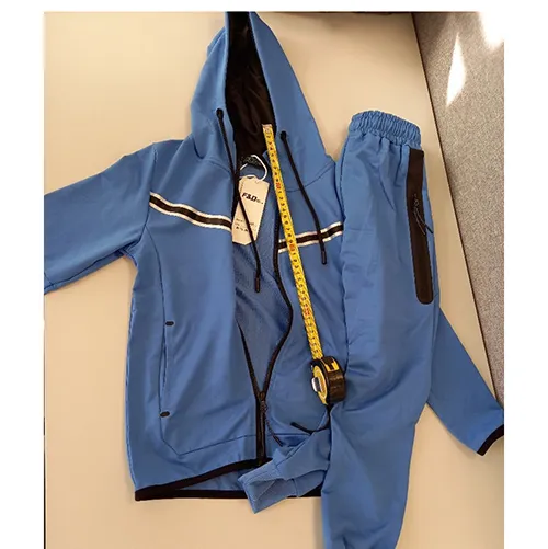 Set de îmbrăcăminte pentru copii destinat copiilor de vârstă mică, confecționat din material tricotat textil albastru deschis. Este compus dintr-un jumper cu glugă, fermoar și buzunare inserate. Capota are un cordon textil funcțional cu șnur, cu capete libere de aproximativ 24 cm lungime. Include, de asemenea, o pereche de pantaloni din material tricotat textil albastru deschis și cu buzunare inserate.