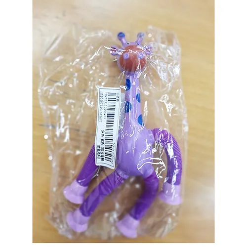 Jucărie de plastic în formă de girafă în violet. Picioarele girafei pot fi extinse și există cupe de aspirație la capetele picioarelor care pot fi atașate la o fereastră, mobilier etc. Produs vândut online, în special prin Shein (identificator unic: sl2501076151622677)