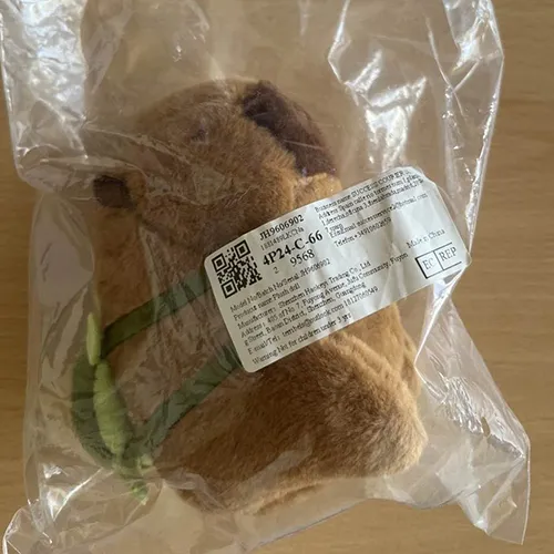 Breloc cu o jucărie moale în formă de capibara maro cu un rucsac textil verde. Produs vândut online, în special prin intermediul Amazon (ASIN: B0CP6VKLGP).