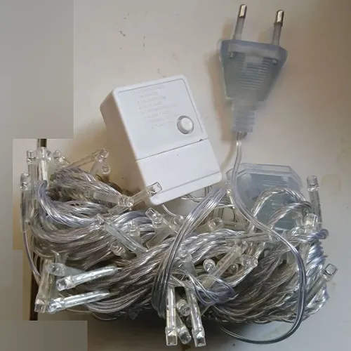 Lanț de iluminat decorativ cu 100 de LED-uri, cablaj transparent și o cutie de control albă integrată (model: EK-04) cu un buton mecanic de selectare a programului pe partea din spate și un conector end-to-end.
