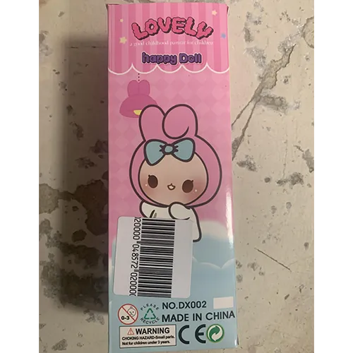 Păpușă din plastic, cu păr sintetic roz, purtând o pălărie textilă cu urechi decorative și îmbrăcată în haine roz.